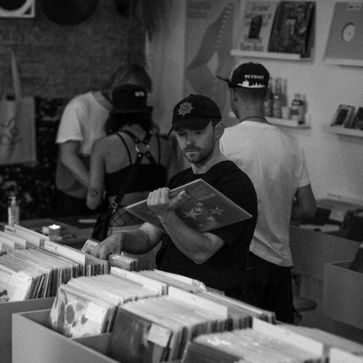 A man in a black cap flipping through a record in a shop, crates of vinyl in front of him