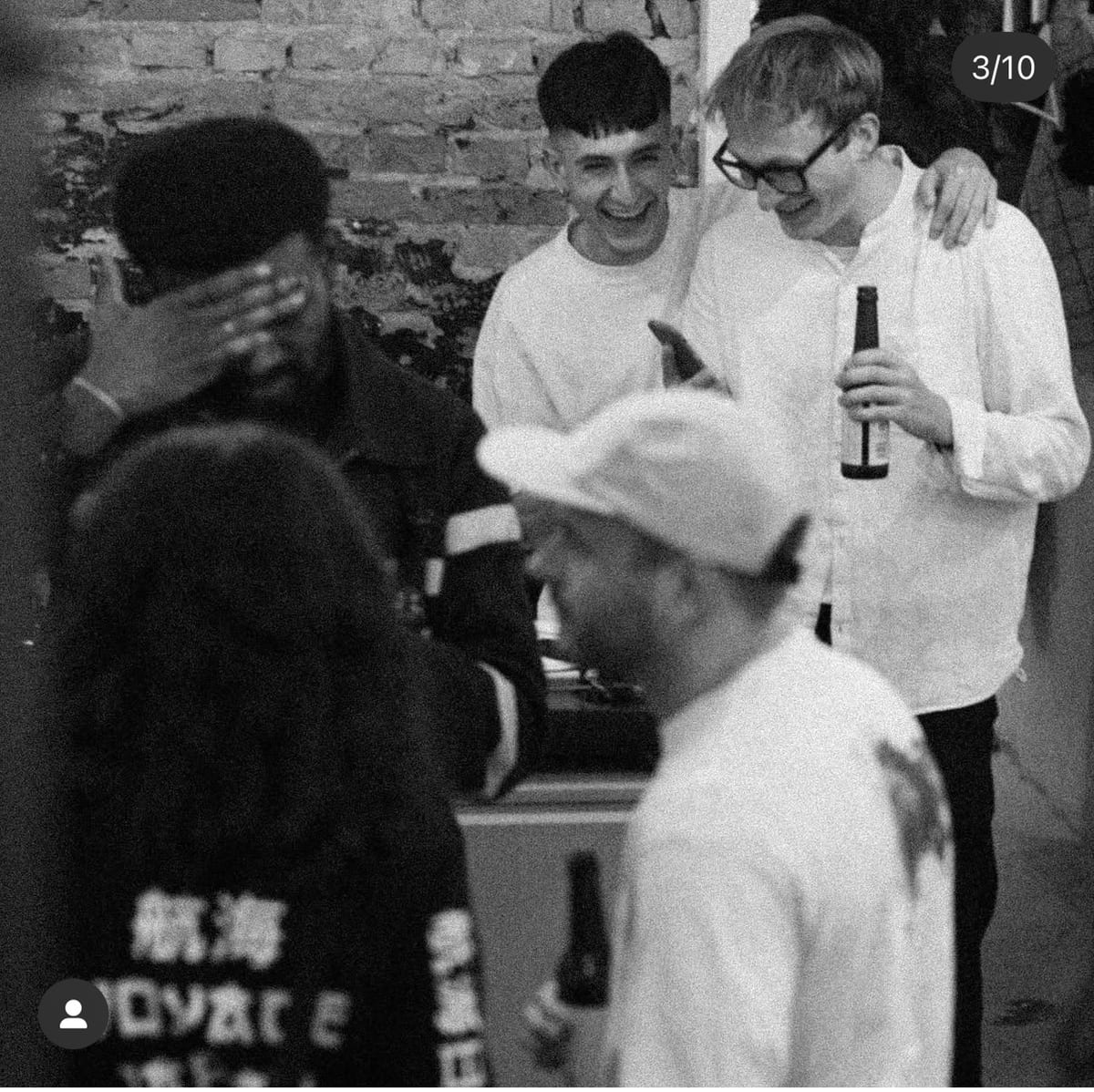 Three friends laughing, beers in hand, in front of a brick wall